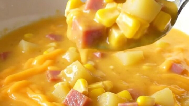 A top-down view of a creamy cheddar chowder filled with ham, corn, and potatoes in a black slow cooker insert.