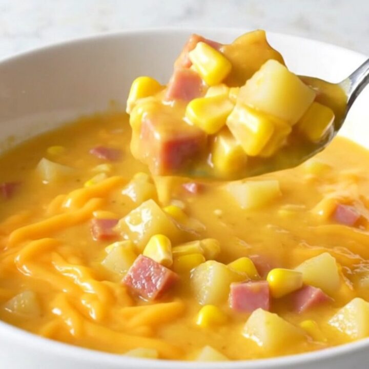 A top-down view of a creamy cheddar chowder filled with ham, corn, and potatoes in a black slow cooker insert.