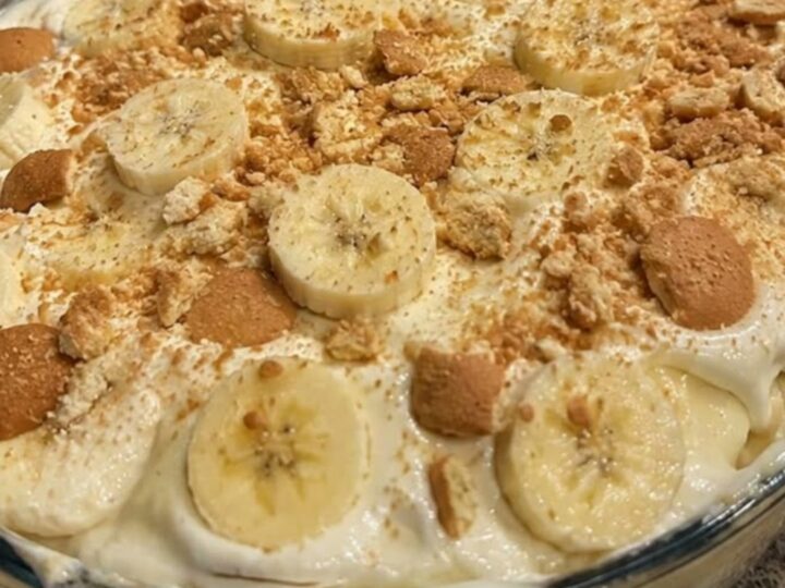 A glass casserole dish filled with layers of banana pudding, topped with banana slices and vanilla wafers.