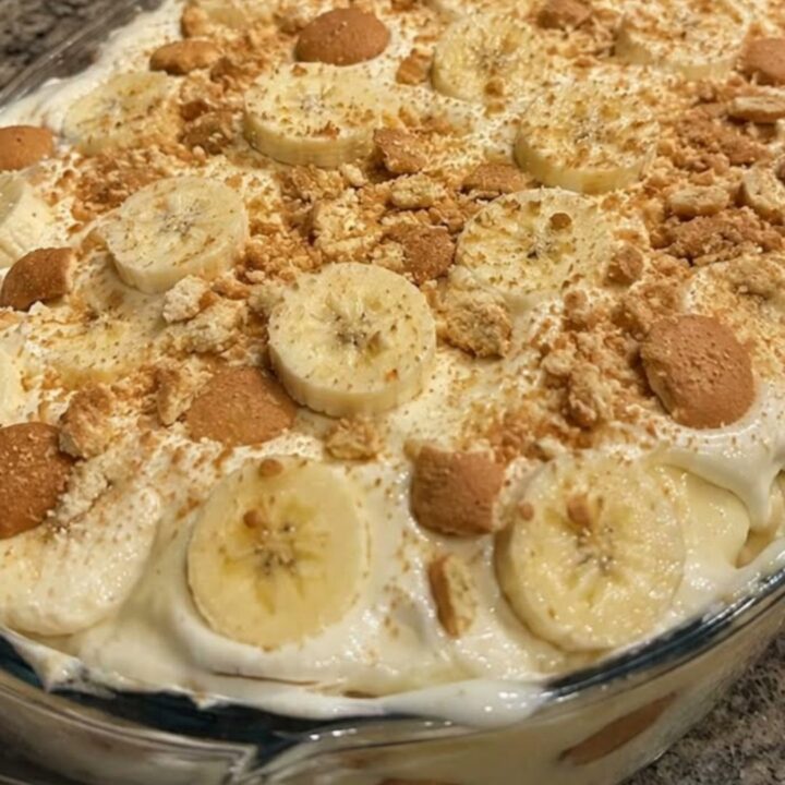 A glass casserole dish filled with layers of banana pudding, topped with banana slices and vanilla wafers.