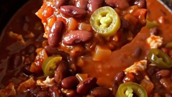 A close-up of a steaming bowl of turkey chili with kidney beans and jalapenos.