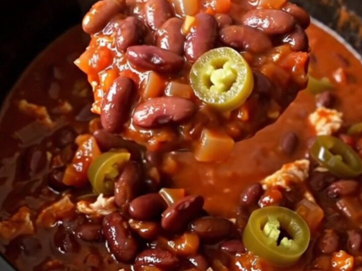 A close-up of a steaming bowl of turkey chili with kidney beans and jalapenos.