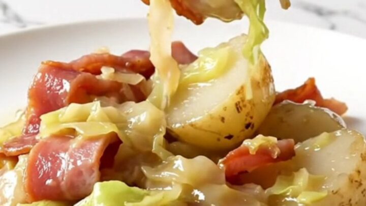 A close-up of a slow cooker filled with layers of Canadian bacon, cabbage, and baby potatoes in a buttery broth.