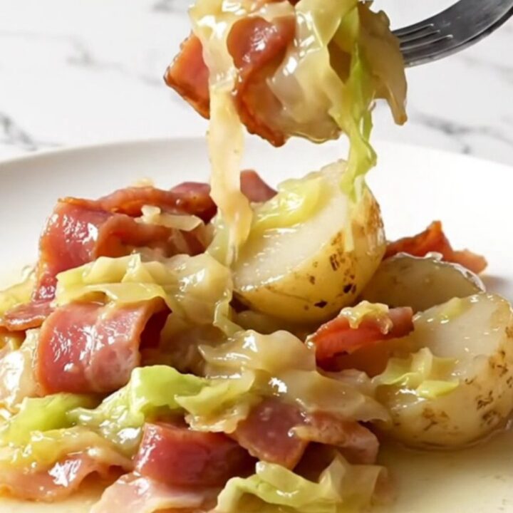 A close-up of a slow cooker filled with layers of Canadian bacon, cabbage, and baby potatoes in a buttery broth.