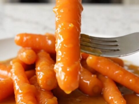 A top-down view of bright orange baby carrots inside a black slow cooker insert with a light dusting of zest and spices.