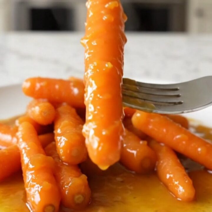 A top-down view of bright orange baby carrots inside a black slow cooker insert with a light dusting of zest and spices.