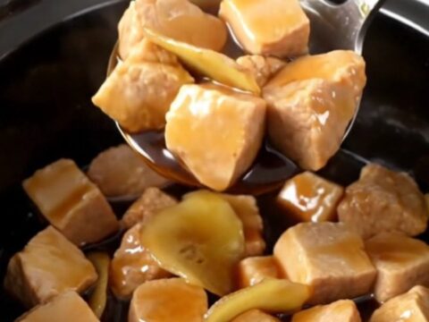 A close-up of tender, glazed pork bites in a slow cooker, featuring a rich dark brown sauce and golden ginger coins.