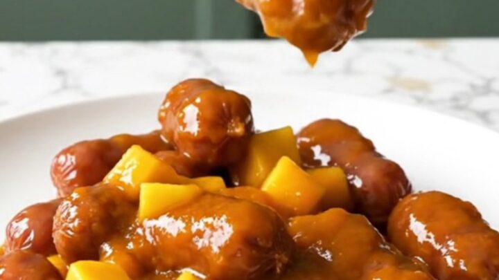 A close-up of mini smoked sausages coated in a glossy orange mango habanero glaze on a white plate.
