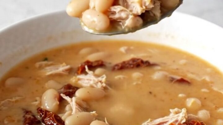 A bowl of creamy Tuscan ground turkey soup with beans and sun-dried tomatoes in a slow cooker.