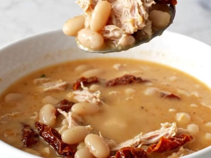 A bowl of creamy Tuscan ground turkey soup with beans and sun-dried tomatoes in a slow cooker.