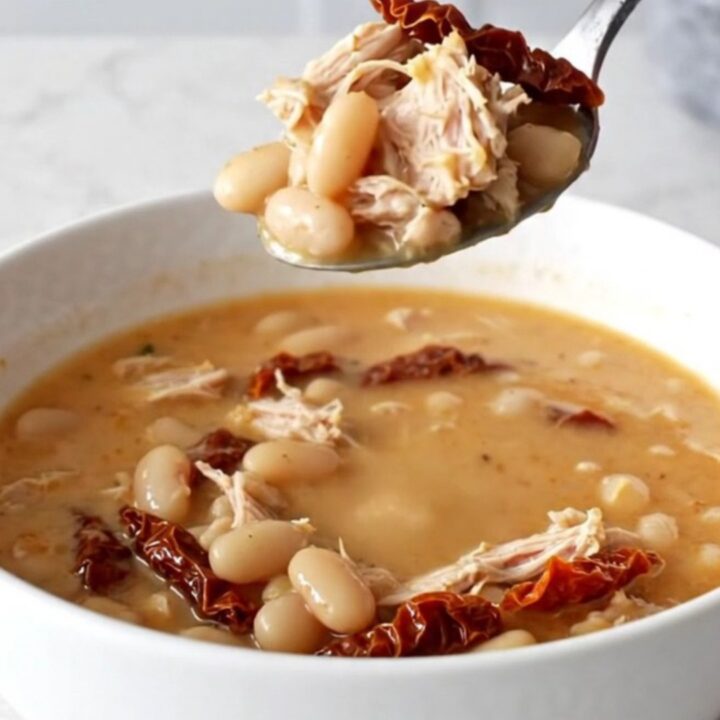 A bowl of creamy Tuscan ground turkey soup with beans and sun-dried tomatoes in a slow cooker.