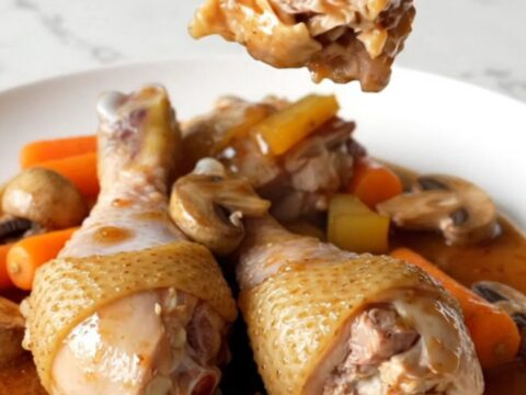 A plate of tender chicken drumsticks with mushrooms and carrots in a rich red wine sauce.