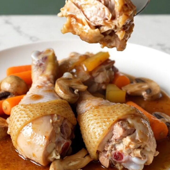 A plate of tender chicken drumsticks with mushrooms and carrots in a rich red wine sauce.