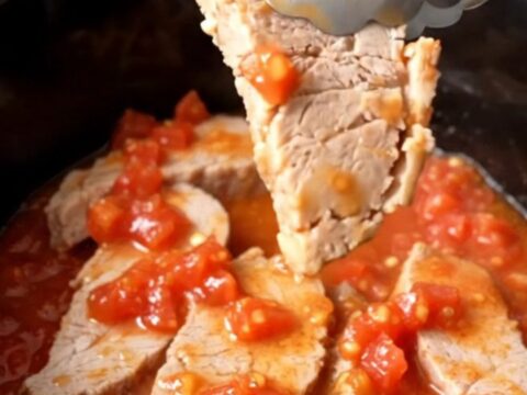A close-up of tender, slow-cooked pork chops covered in a rich tomato, onion, and okra sauce in a black slow cooker insert.