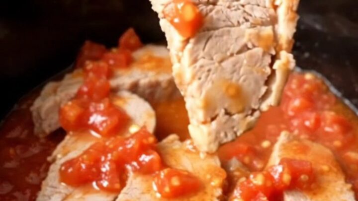 A close-up of tender, slow-cooked pork chops covered in a rich tomato, onion, and okra sauce in a black slow cooker insert.