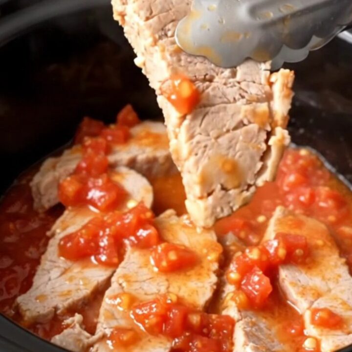 A close-up of tender, slow-cooked pork chops covered in a rich tomato, onion, and okra sauce in a black slow cooker insert.