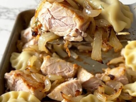 A sheet pan filled with roasted pierogies, golden chicken breast chunks, and soft onions with fresh green dill.