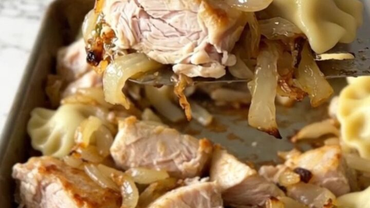 A sheet pan filled with roasted pierogies, golden chicken breast chunks, and soft onions with fresh green dill.