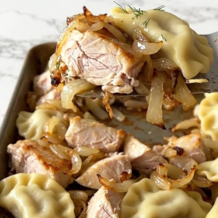 A sheet pan filled with roasted pierogies, golden chicken breast chunks, and soft onions with fresh green dill.