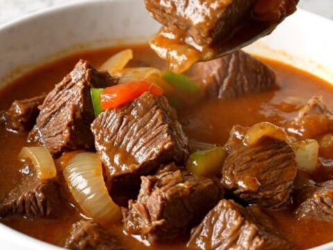 A rustic bowl of slow-cooked Swiss steak stew with tender beef, onions, and bright green peppers in a rich red tomato sauce.