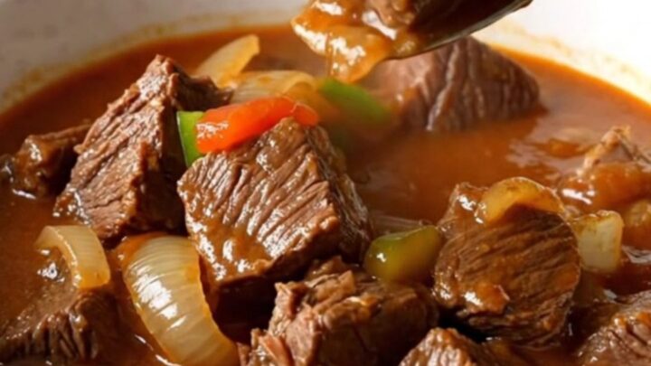A rustic bowl of slow-cooked Swiss steak stew with tender beef, onions, and bright green peppers in a rich red tomato sauce.