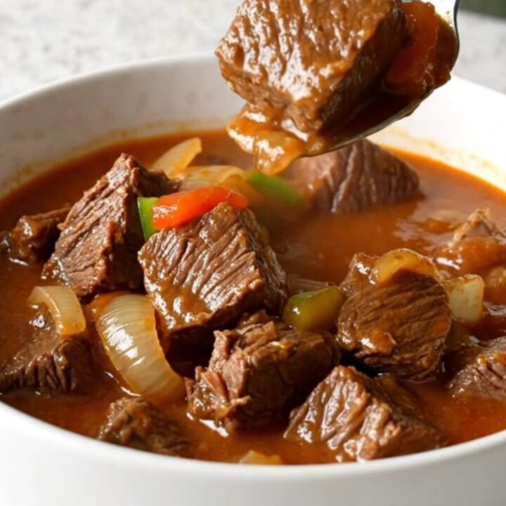 A rustic bowl of slow-cooked Swiss steak stew with tender beef, onions, and bright green peppers in a rich red tomato sauce.