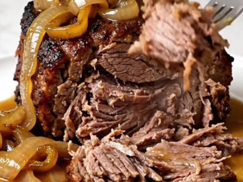 A close-up of a tender, slow-cooked beef chuck roast topped with banana peppers and onions on a white plate.