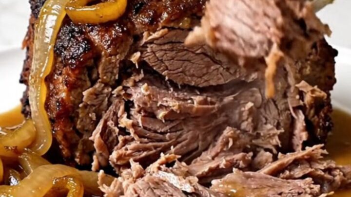 A close-up of a tender, slow-cooked beef chuck roast topped with banana peppers and onions on a white plate.