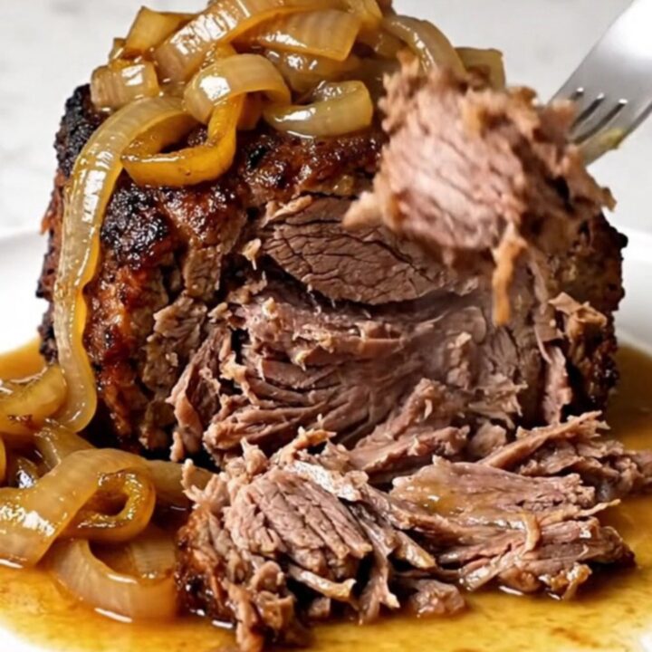 A close-up of a tender, slow-cooked beef chuck roast topped with banana peppers and onions on a white plate.