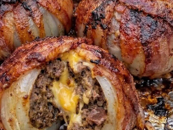 A close-up of a sliced bacon-wrapped onion bomb revealing a molten cheddar cheese center and juicy beef.