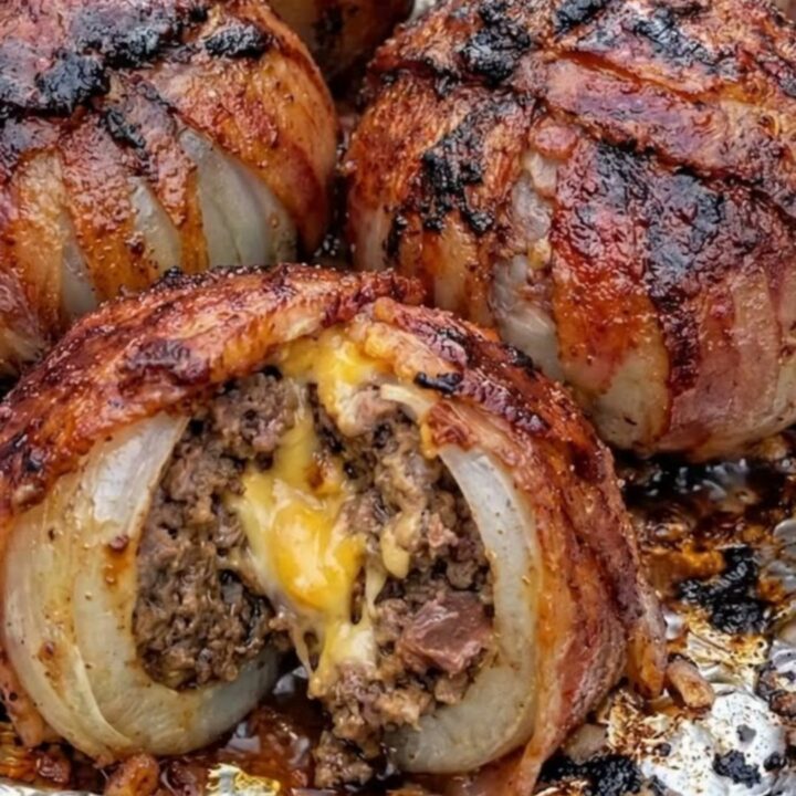 A close-up of a sliced bacon-wrapped onion bomb revealing a molten cheddar cheese center and juicy beef.
