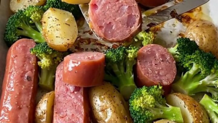 A sheet pan filled with roasted kielbasa coins, golden baby potatoes, and broccoli, topped with everything bagel seasoning.