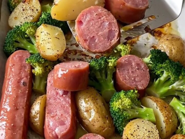 A sheet pan filled with roasted kielbasa coins, golden baby potatoes, and broccoli, topped with everything bagel seasoning.
