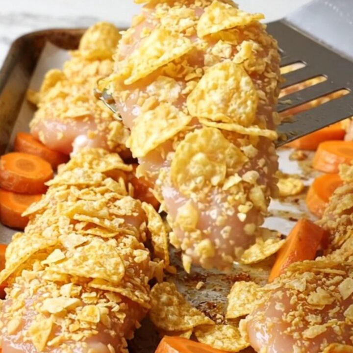Crispy chicken tenders with a golden potato chip crust and roasted carrot coins on a sheet pan.