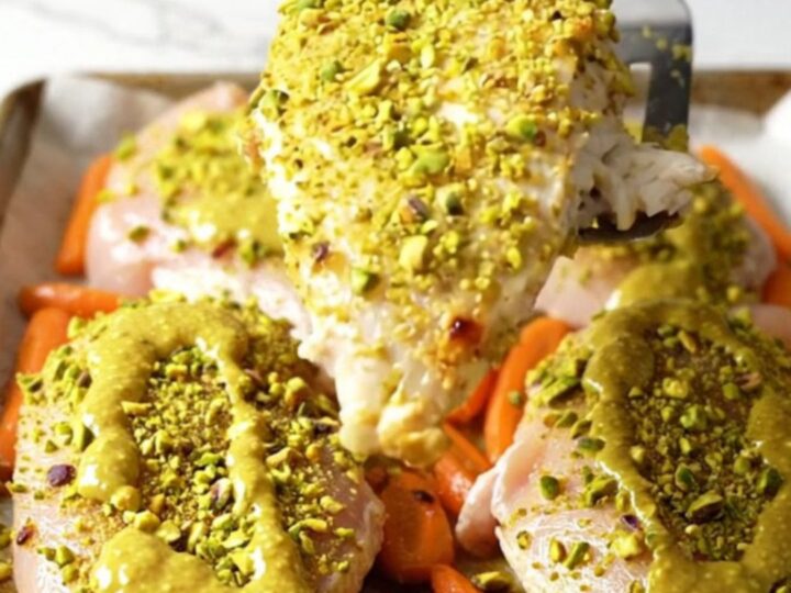 A sheet pan filled with perfectly roasted chicken breasts topped with a vibrant green pistachio crust and golden orange