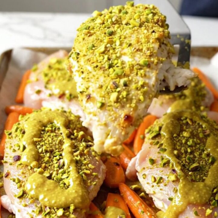A sheet pan filled with perfectly roasted chicken breasts topped with a vibrant green pistachio crust and golden orange