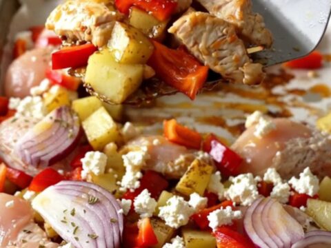 A sheet pan filled with golden-brown chicken breast chunks, roasted potatoes, bell peppers, and melted feta cheese.