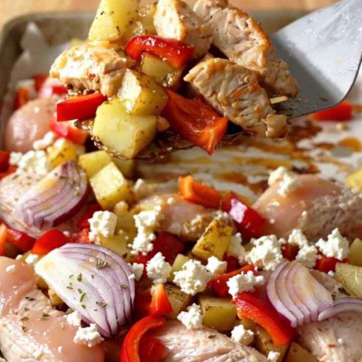 A sheet pan filled with golden-brown chicken breast chunks, roasted potatoes, bell peppers, and melted feta cheese.