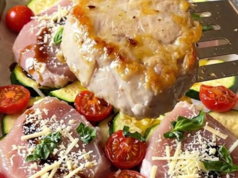 Sheet pan featuring golden-brown pork medallions, roasted zucchini, and blistered cherry tomatoes.