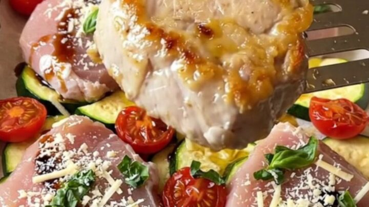 Sheet pan featuring golden-brown pork medallions, roasted zucchini, and blistered cherry tomatoes.