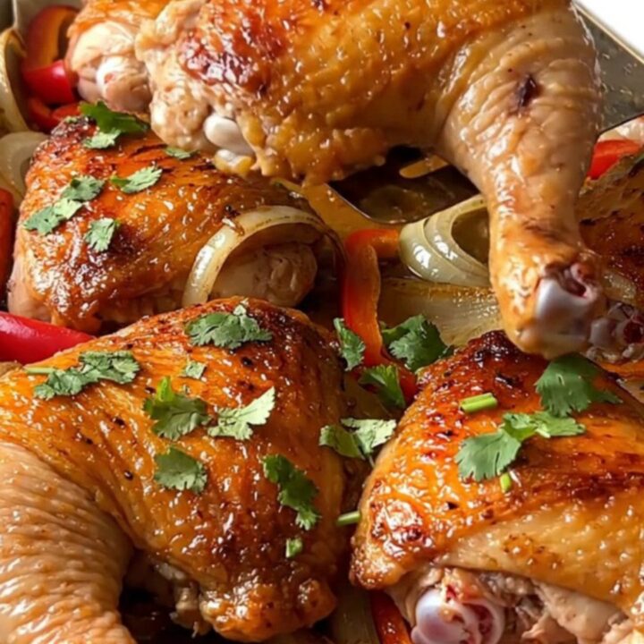 A sheet pan filled with golden-brown roasted chicken thighs, red pepper strips, and white onion wedges.