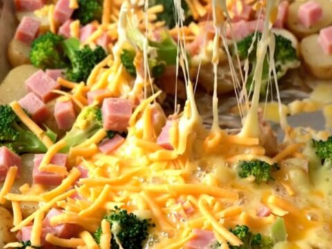A golden sheet pan filled with roasted ham, broccoli, and potatoes covered in melted, bubbly cheddar cheese.