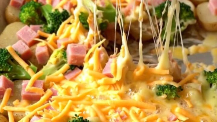 A golden sheet pan filled with roasted ham, broccoli, and potatoes covered in melted, bubbly cheddar cheese.