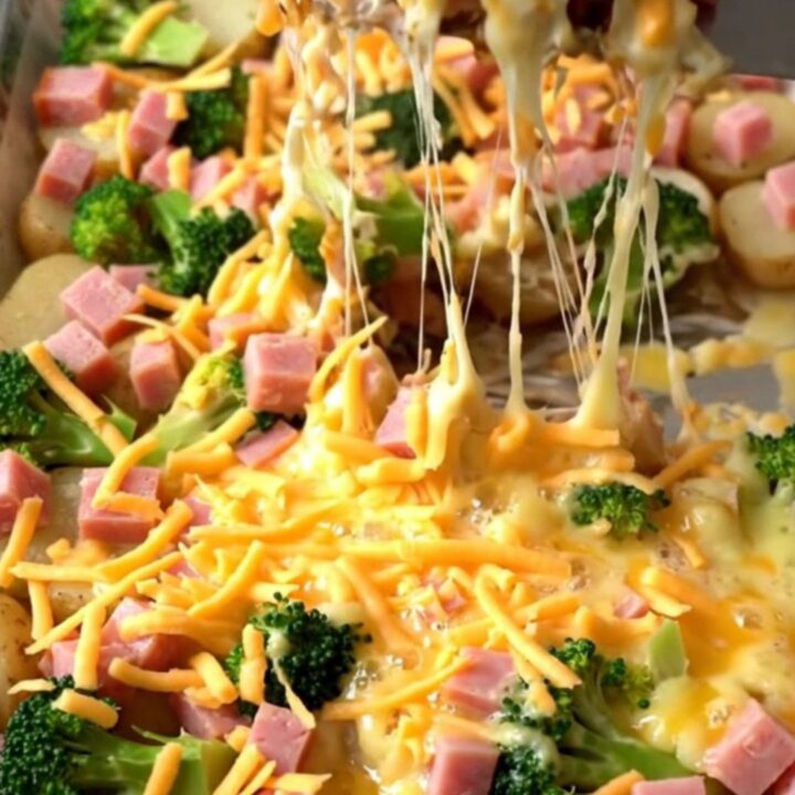 A golden sheet pan filled with roasted ham, broccoli, and potatoes covered in melted, bubbly cheddar cheese.