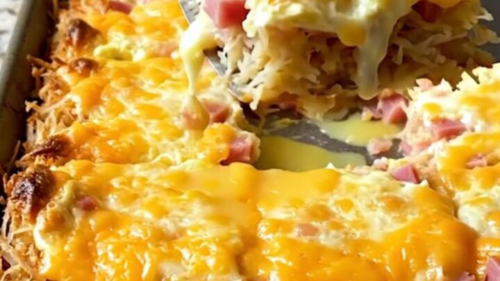 A golden, square-cut slice of sheet pan eggs with visible crispy hash browns, diced ham, and melted pepper jack cheese.