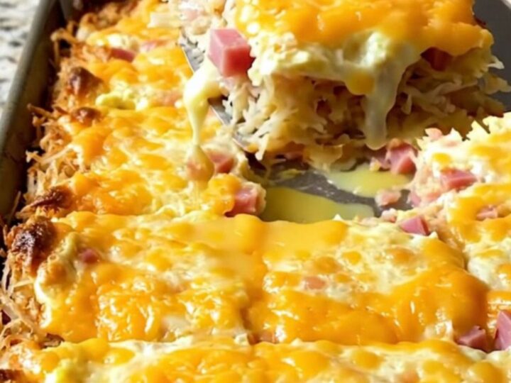 A golden, square-cut slice of sheet pan eggs with visible crispy hash browns, diced ham, and melted pepper jack cheese.