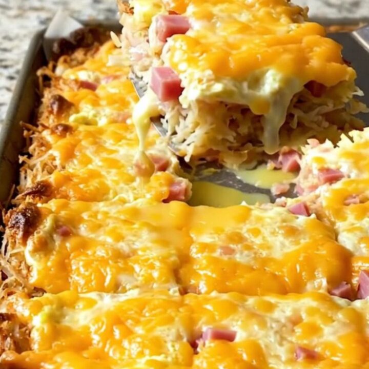 A golden, square-cut slice of sheet pan eggs with visible crispy hash browns, diced ham, and melted pepper jack cheese.