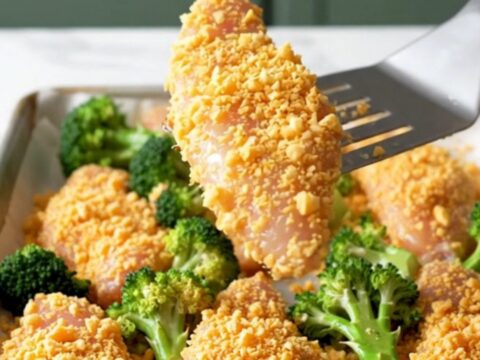 A sheet pan filled with golden-brown cracker-crusted chicken tenders and roasted green broccoli florets.