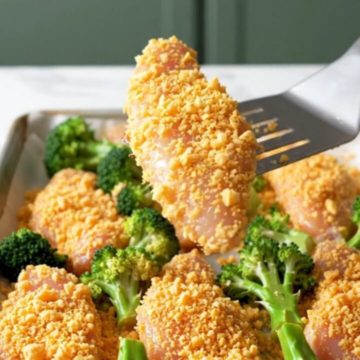 A sheet pan filled with golden-brown cracker-crusted chicken tenders and roasted green broccoli florets.