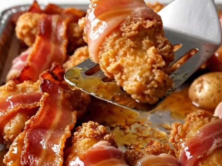 A sheet pan filled with bacon-wrapped chicken tenders and golden roasted baby potatoes drizzled with maple syrup.